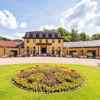 Landschaftsaufnahme mit Hofmarschallamt und kleinem bepflanzten Teppichbeet im Schlosspark Altenstein
