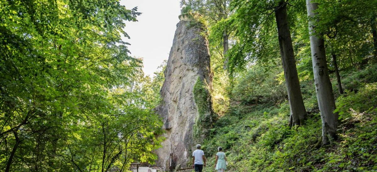 Landschaftsaufnahme mit Menschen, hohem, spitzen Felsen, darauf ein bepflanzter Blumenkorb im Schlosspark Altenstein